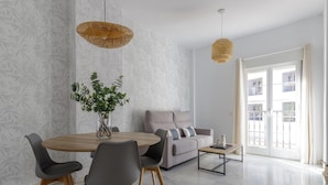 Una sala de estar moderna con una mesa de comedor, sillas, un sofá y un balcón con ventanas decoradas.