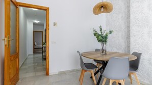 Un comedor con una mesa redonda de madera, sillas grises, una lámpara colgante y una planta en maceta.