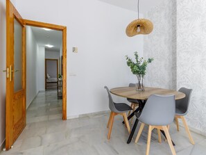 A dining area with a round wooden table, grey chairs, a hanging light fixture, and a potted plant. - Urban Chic 3A - 1 dorm Living4malaga (Distrito Centro)