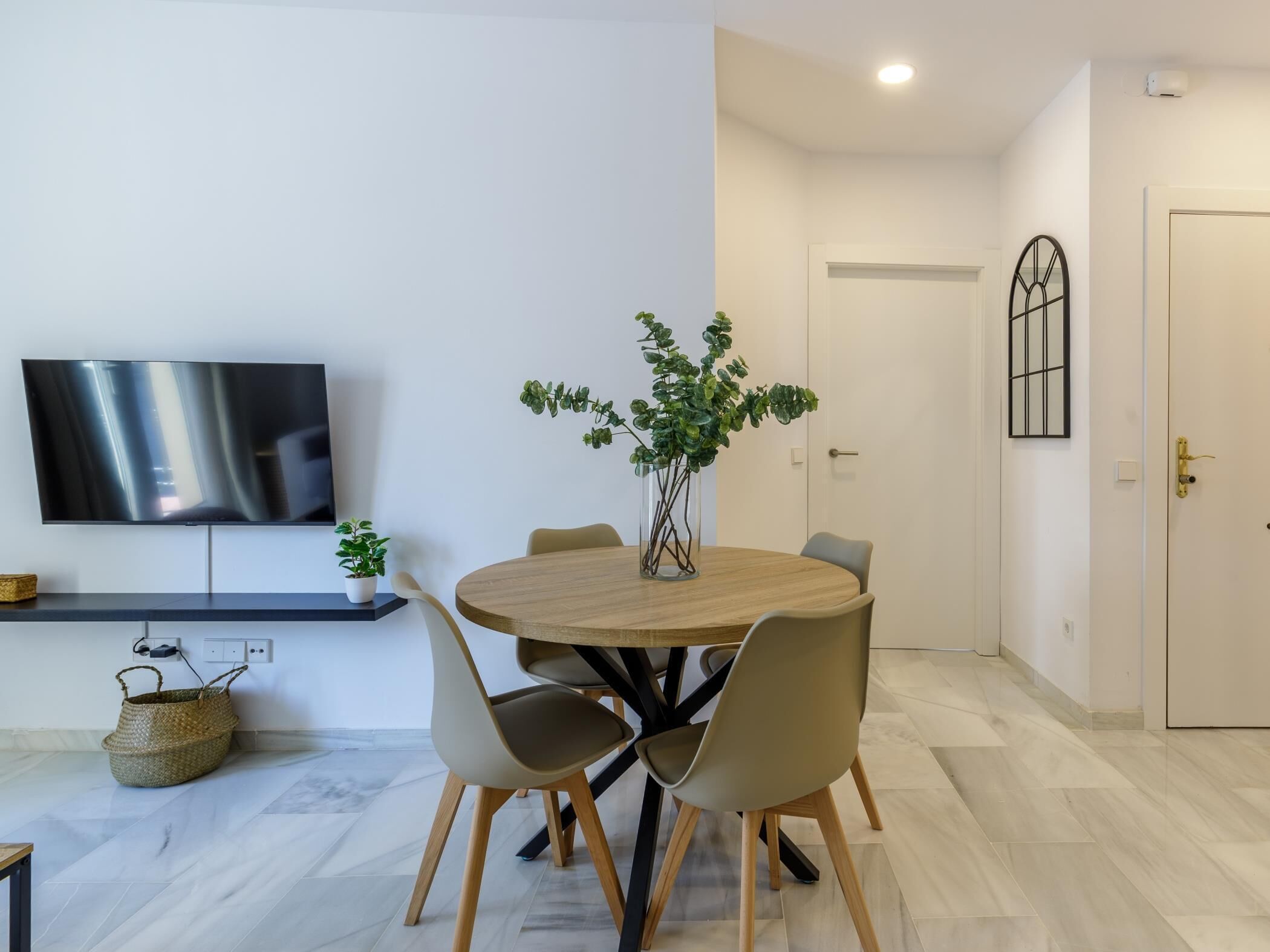 A modern dining area with a round table, chairs, a TV, and a potted plant.