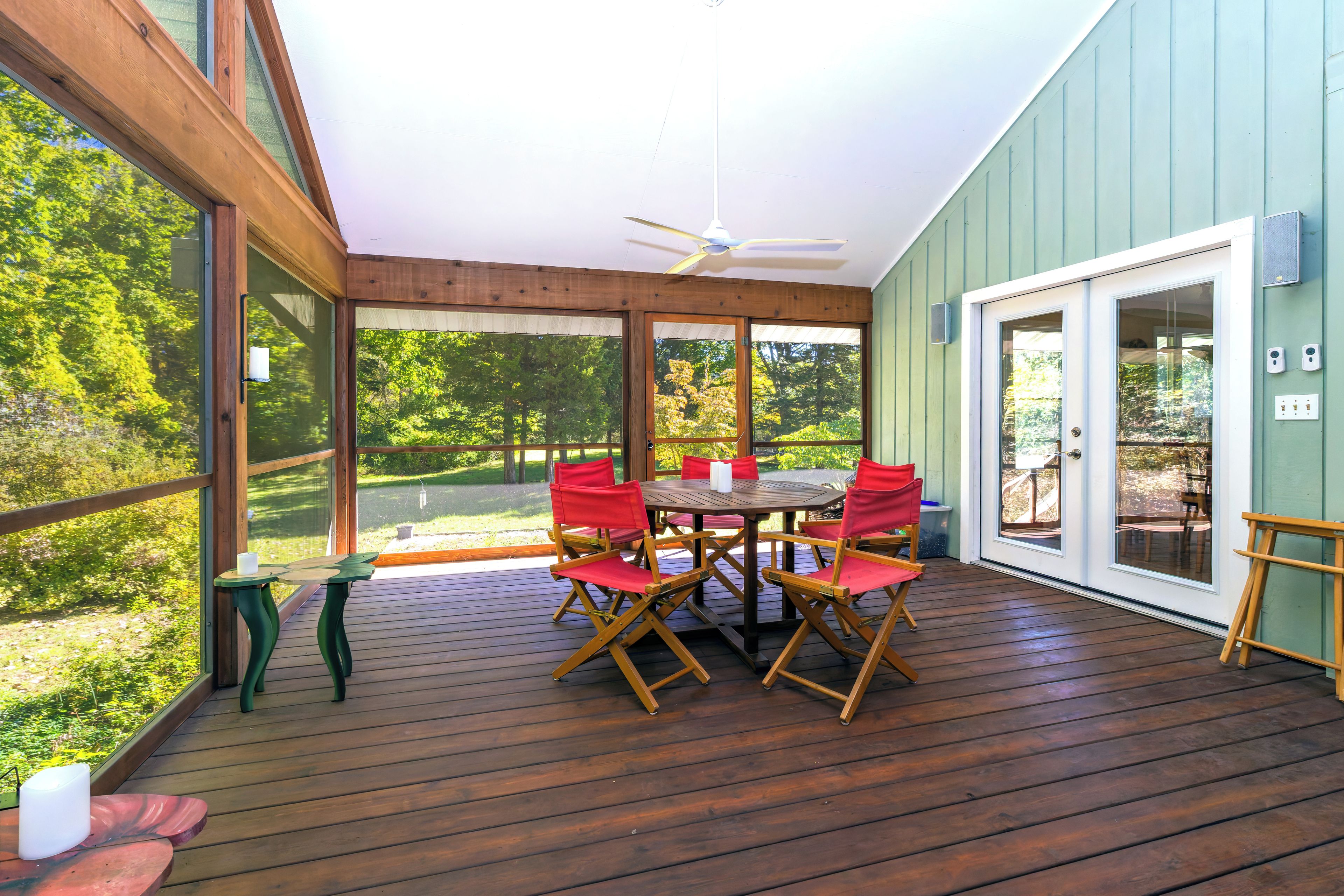 A covered outdoor patio with a table and chairs, large windows, and a ceiling fan.