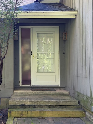 A front door with a glass panel, a small step leading up to it, and a wooden handrail. - Forest Hideaway- Hot tub- close to Lake Michigan (South Haven)