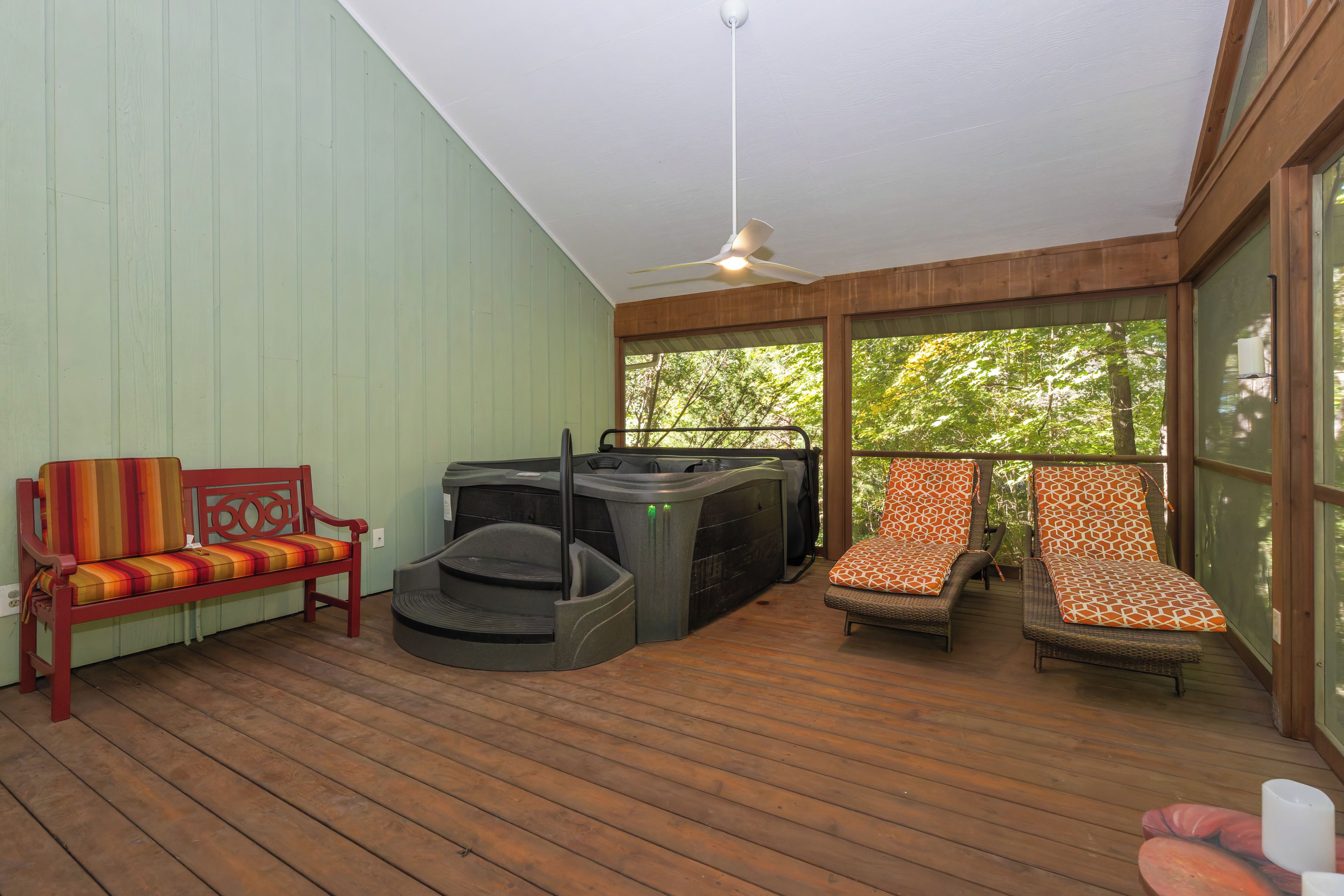 A wooden deck with a bench, a hot tub, and two lounge chairs.