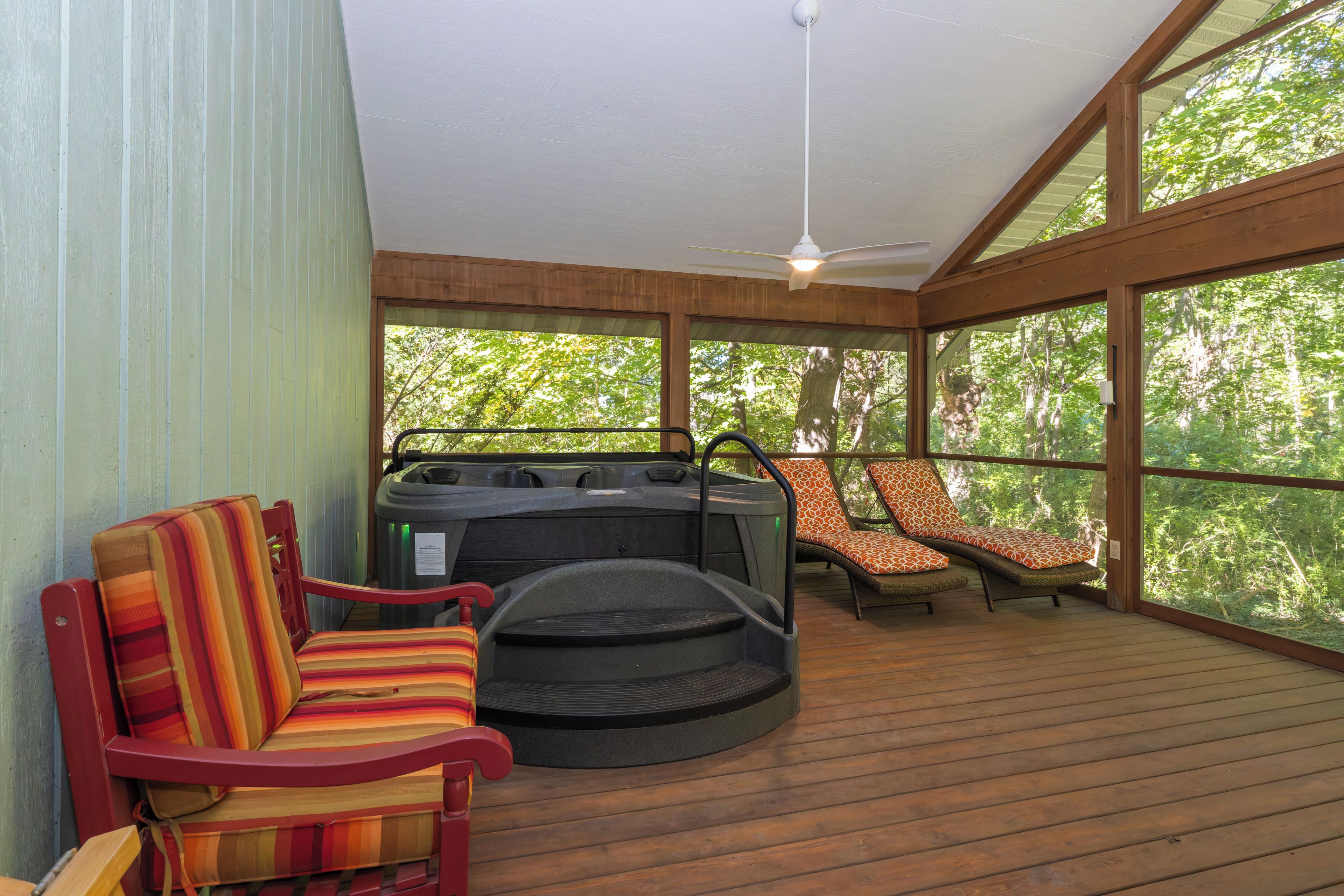 A covered outdoor seating area with a hot tub, lounge chairs, and a ceiling fan.