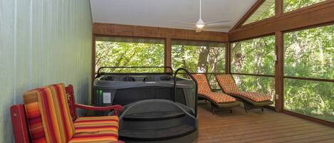 A covered outdoor seating area with a hot tub, lounge chairs, and a ceiling fan.