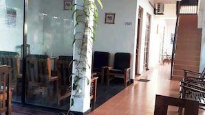 A spacious indoor area with a long wooden table and several chairs, a large pillar with a plant, and a glass wall with reflections. - Hotel City Esala (Dambulla)