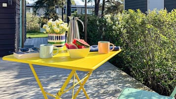 A yellow outdoor table with a pitcher, a bowl of fruit, a mug, and a book.