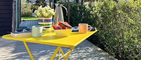 A yellow outdoor table with a pitcher, a bowl of fruit, a mug, and a book.