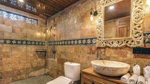 Un baño con inodoro, lavabo de cuenca grande, ducha y espejo con marco decorativo.