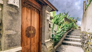 Una puerta de madera con tallas intrincadas, una escalera de piedra y abundante vegetación.