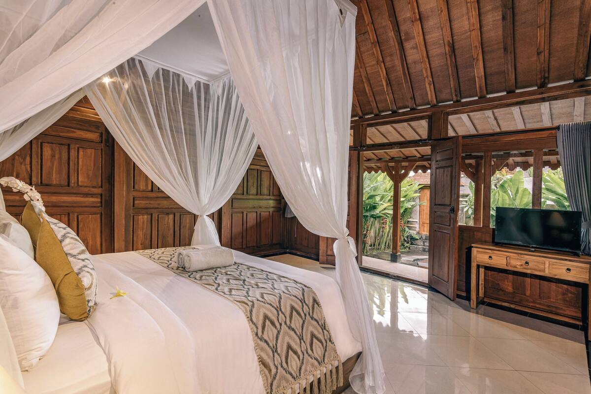 Ein Schlafzimmer mit Baldachinbett, Holzwänden, einem Fernseher auf einer Holzkommode und Blick auf Grünfläche.