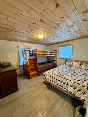 Una cama litera de madera con escalera, un escritorio y una ventana con persianas.