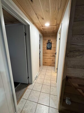 Ein schmaler Korridor mit Holzboden und Fliesenboden, der zu einem Raum mit einer Tür und einem an der Wand befestigten Gegenstand führt.