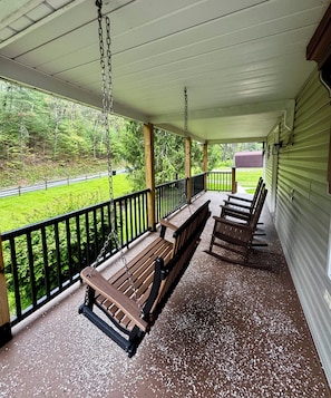 Eine überdachte Veranda mit hölzernen Bänken und einer Schaukel, mit Blick auf eine grüne Landschaft.