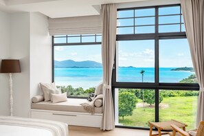 Ein Schlafzimmer mit großem Fenster, Bett, Nachttischlampe und Blick auf das Meer und die Berge.