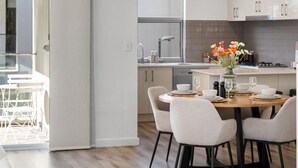 A modern kitchen with white cabinets, a dining area with a round table and chairs, and a view of the outdoors through a sliding door. - Loft & Levels @ Prospect - Contemporary Urban Living (Prospect)