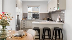 A modern kitchen with white cabinets, a central island, black stools, and a dining table set with glassware and plates. - Loft & Levels @ Prospect - Contemporary Urban Living (Prospect)