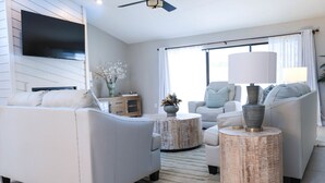 Ein modernes Wohnzimmer mit einem an der Wand montierten Flachbildfernseher, zwei Sofas, einem Couchtisch und einem Beistelltisch mit Lampe.