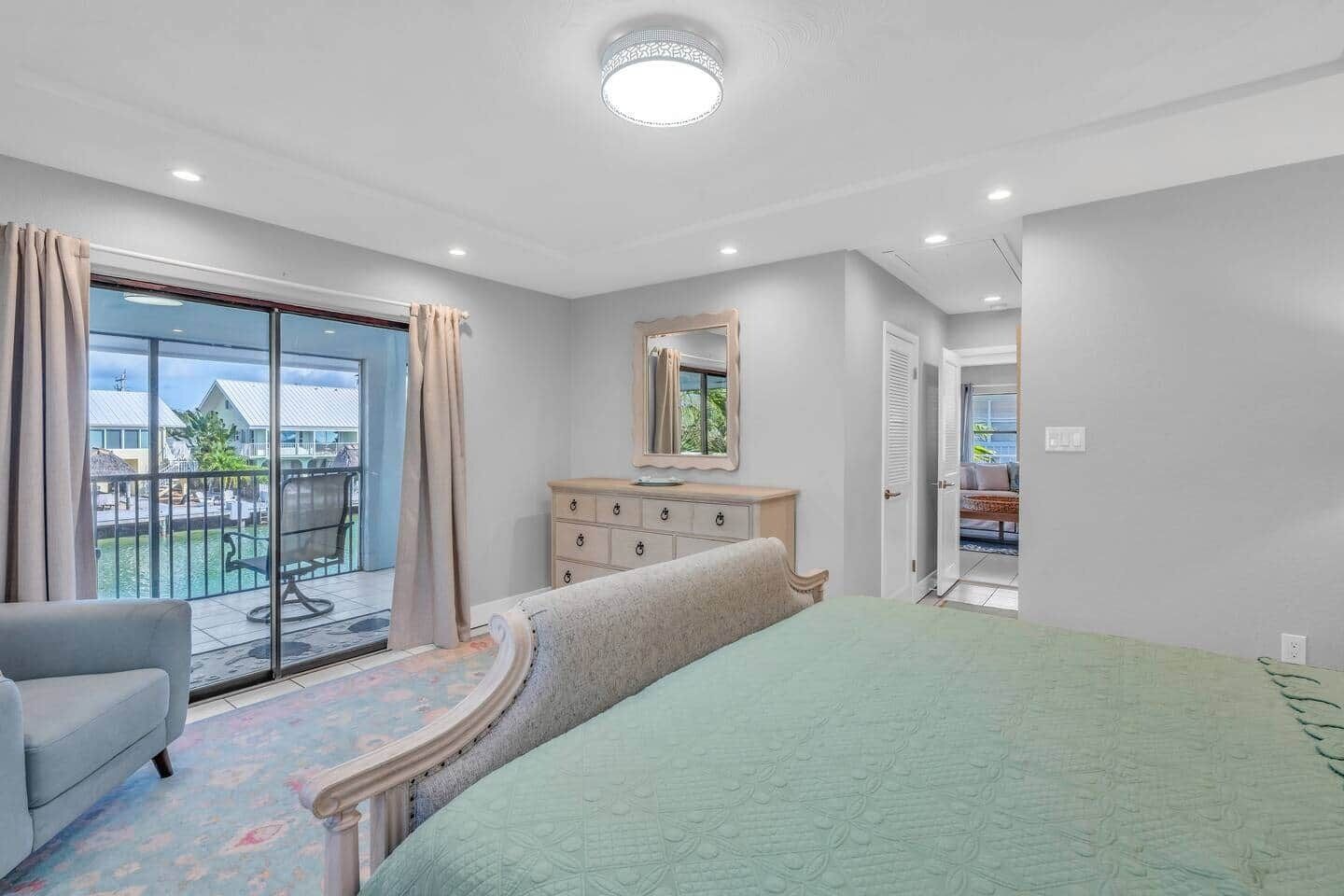 A bedroom with a large bed, a dresser, a mirror, and a view of a pool and outdoor area.