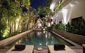 Zona de piscina con sillones de descanso y vista a un edificio de estilo arquitectónico tradicional.