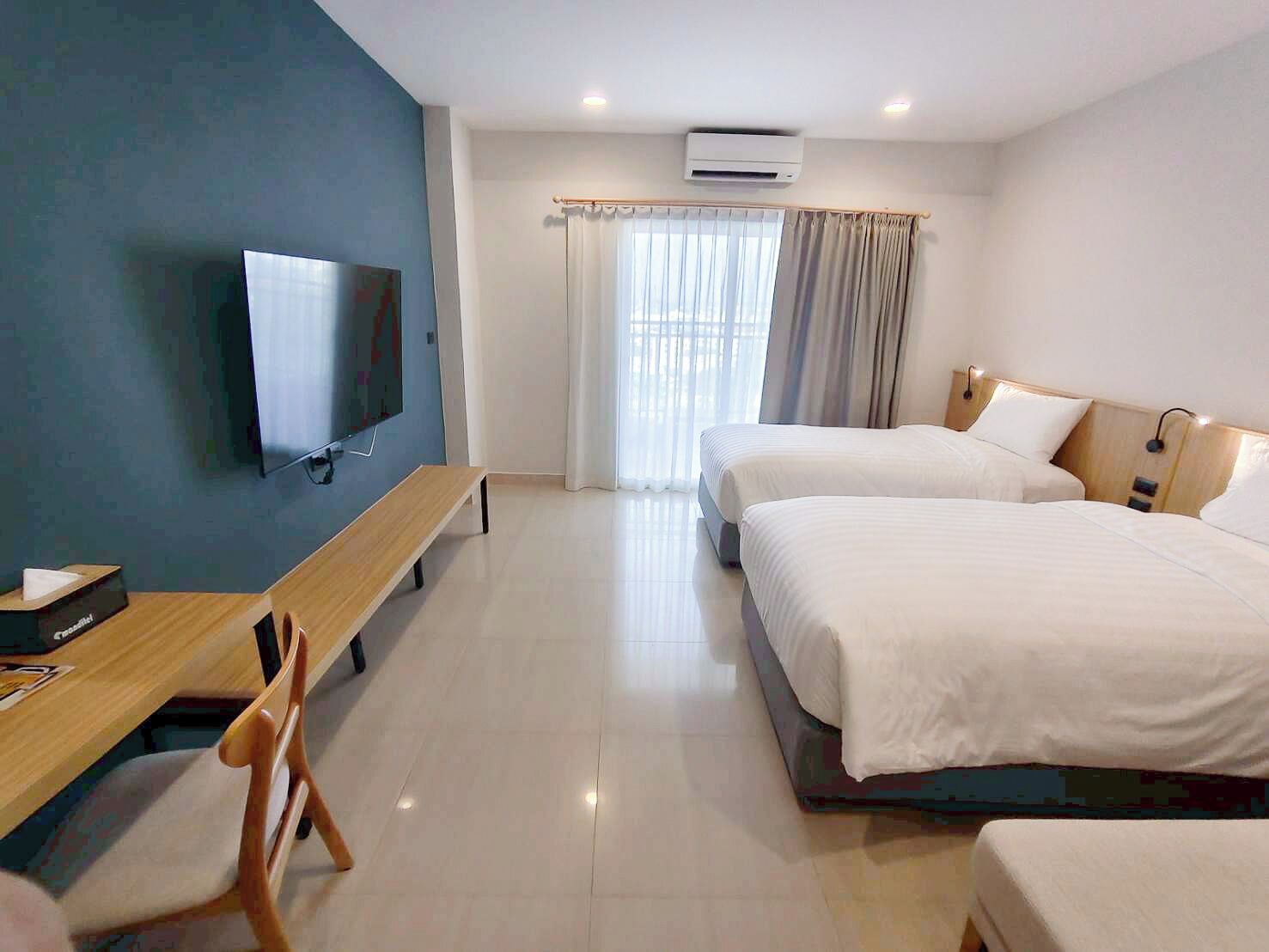 Ein Hotelzimmer mit Fernseher, zwei Betten, einem Schreibtisch und einem Stuhl.