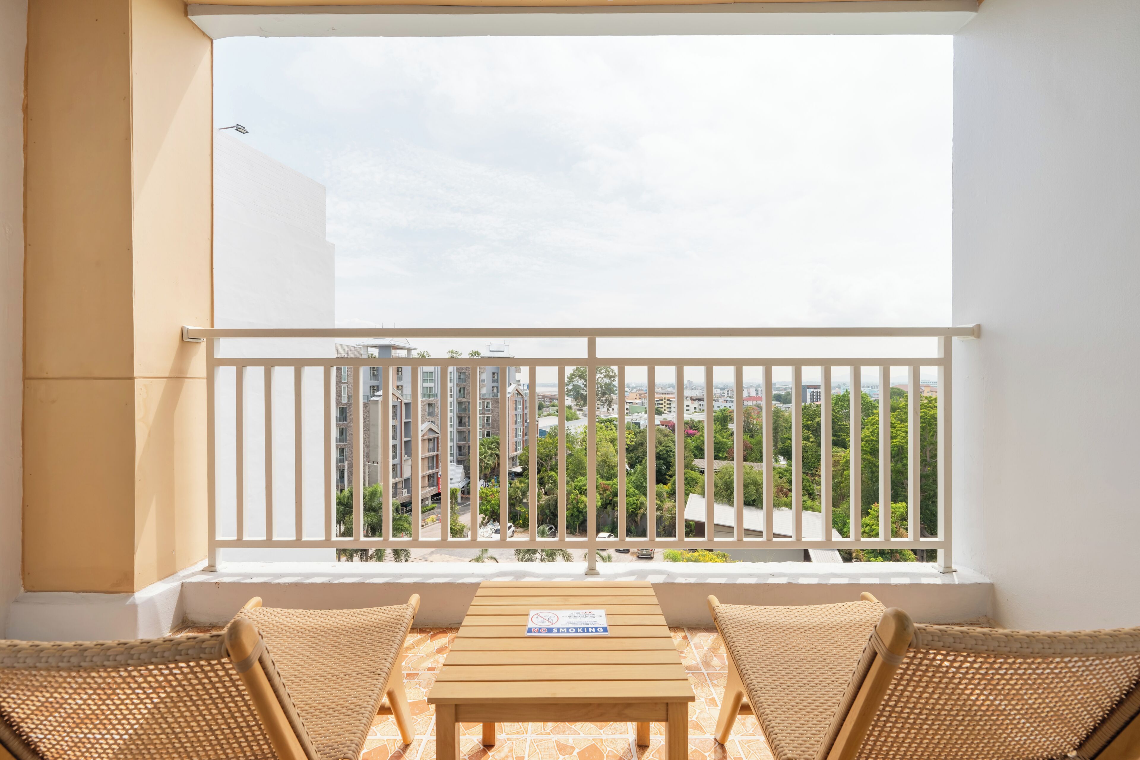 A balcony with wicker furniture, a table, and a view of buildings and greenery.