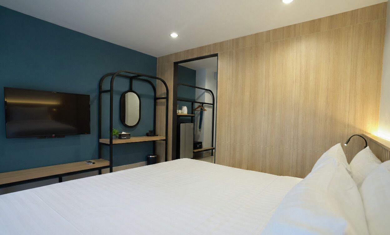 A modern hotel room with a bed, a TV mounted on the wall, a wooden wardrobe, and a mirror.