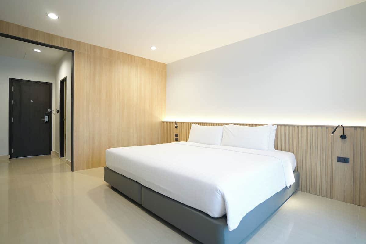 Un dormitorio moderno con una cama grande, paneles de madera en las paredes y una lámpara de techo luminosa.