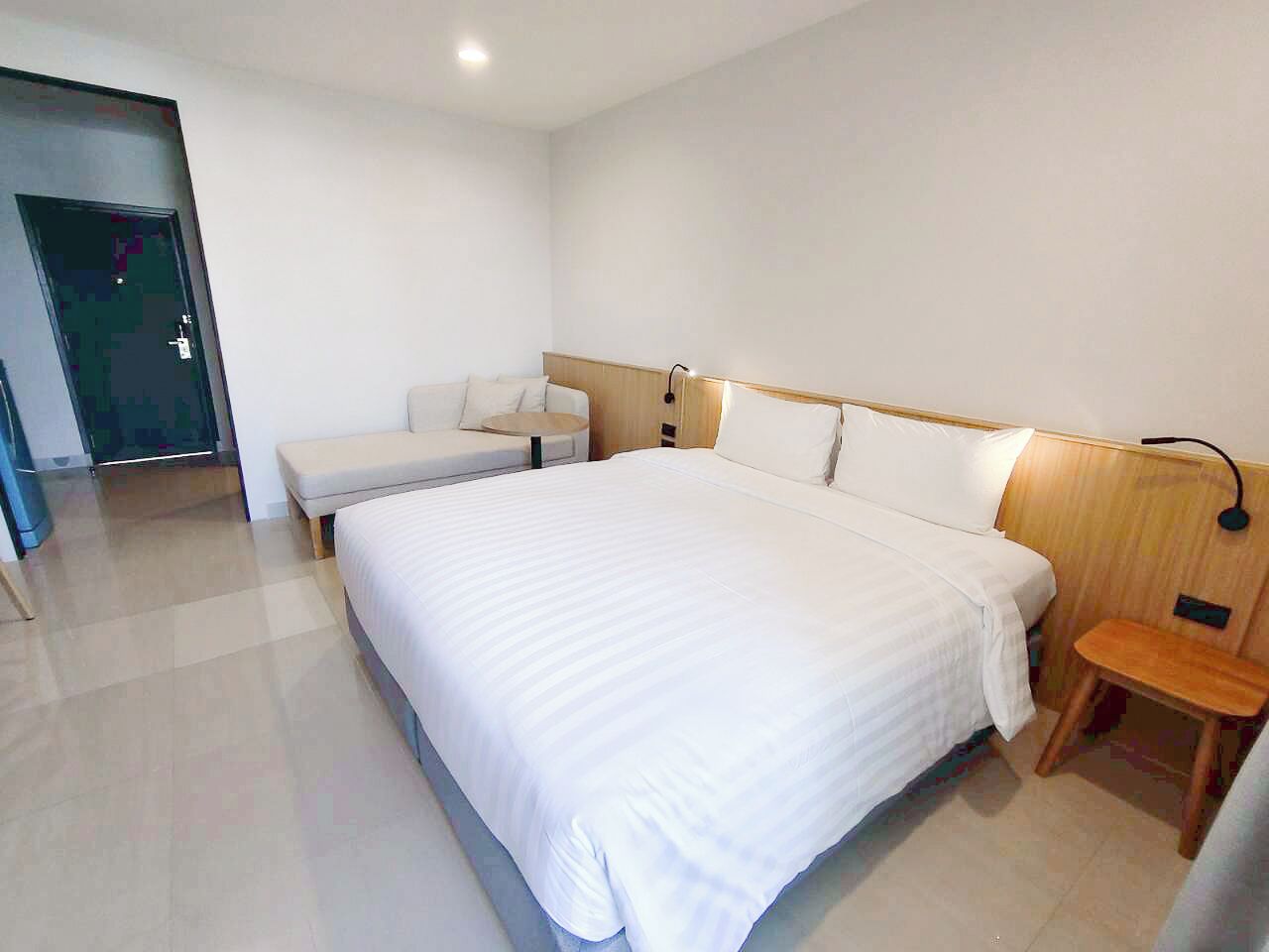 A modern hotel room with a large bed, a bedside table, a chair, and a nightstand.
