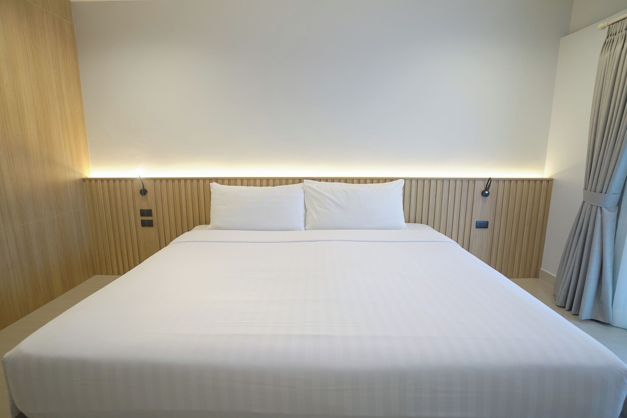 Ein großes, ordentlich bezogenes Bett mit weißen Leinentüchern, einem Holz-Kopfstück und einer Wandleuchte.