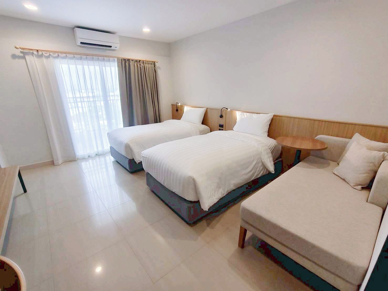 Habitación de hotel con dos camas, una mesita y un sofá.