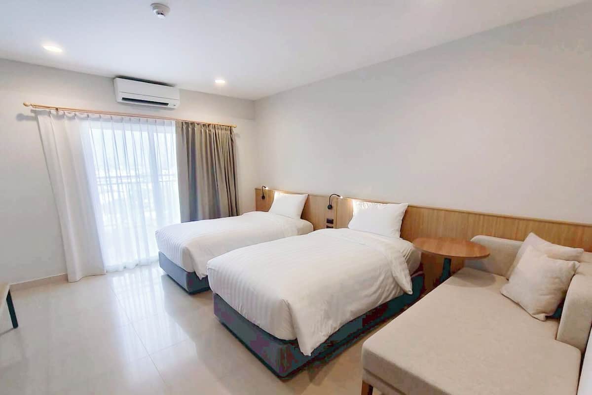 Una habitación de hotel con dos camas, un sofá, una mesita y una ventana con cortinas.