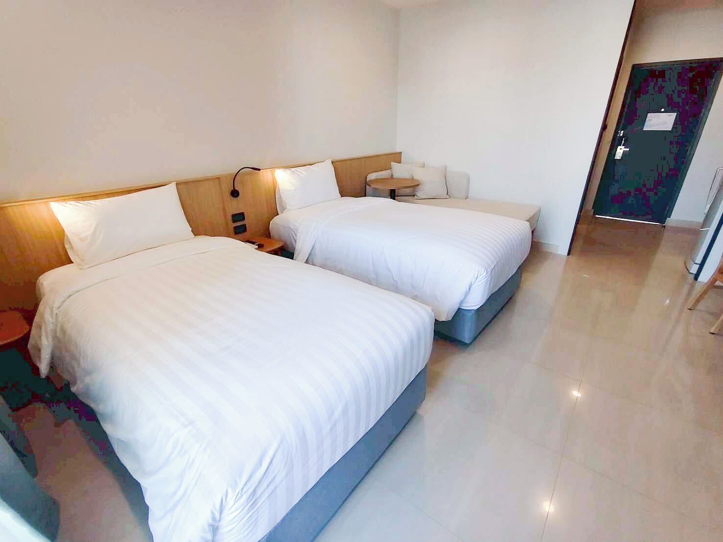 A hotel room with two beds, a bedside table, a small round table, and a door with a purple pattern.