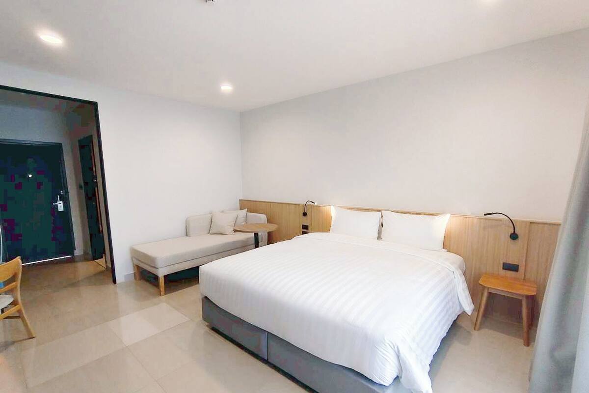 Una habitación de hotel moderna con una cama grande, un sofá, una mesita y una silla.