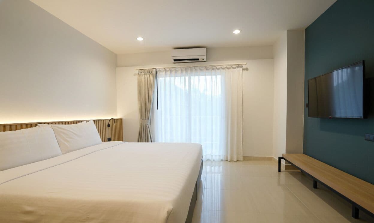 A hotel room with a large bed, a bench, a flat-screen TV, and a window with curtains.