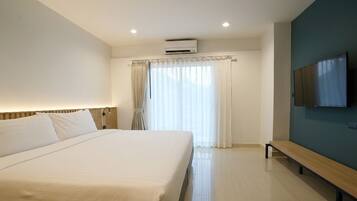 A hotel room with a large bed, a bench, a flat-screen TV, and a window with curtains.