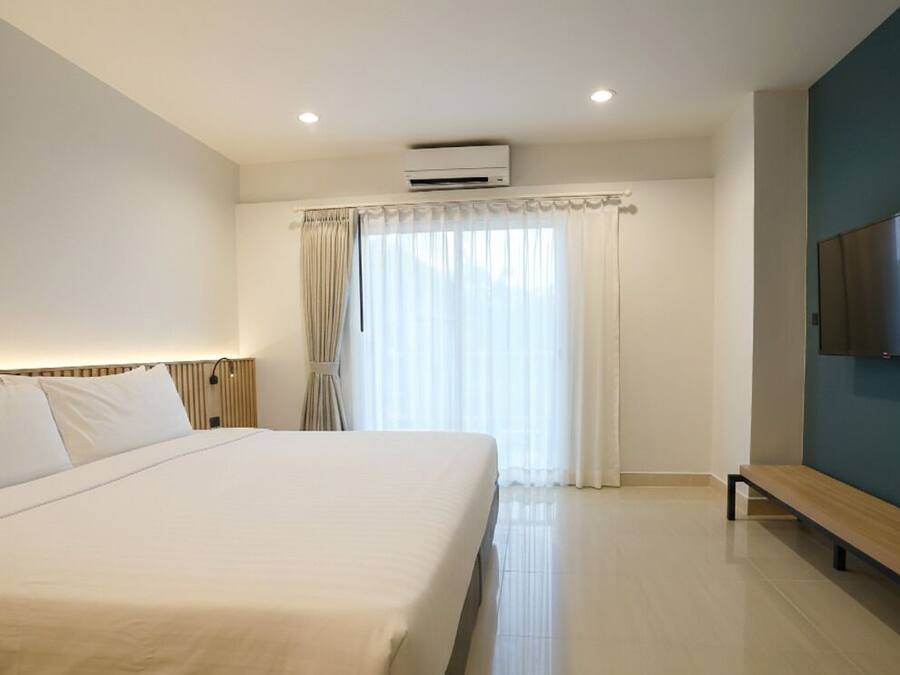 A hotel room with a large bed, a bench, a flat-screen TV, and a window with curtains.