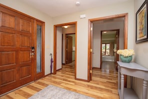 A hallway with wooden floors, a door with a metal handle, and a vase with flowers on a console table.