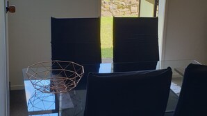 A dining area with a glass table and chairs, a view of greenery and mountains through a window, and a partially open door. - Lazy Daze at Athenree with local hot pools, and only 5 minutes from Waihi Beach (Athenree)
