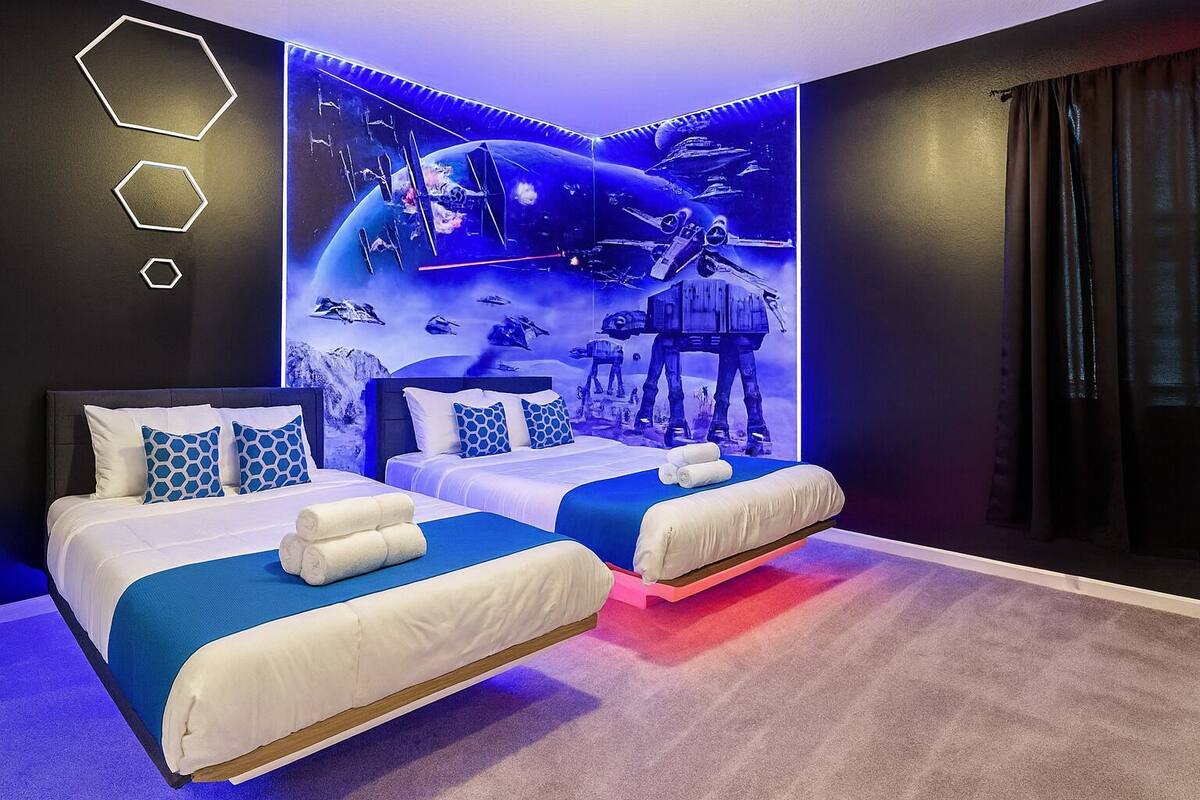 Camera d'albergo con due letti, un grande murale a tema spaziale e un design moderno.
