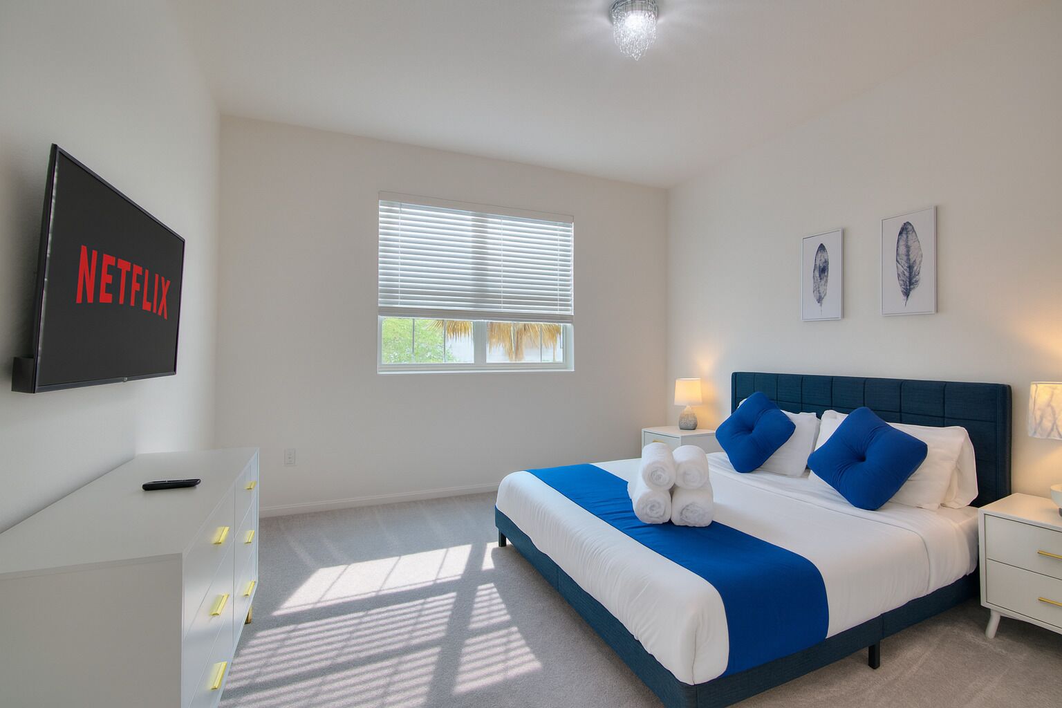 A bedroom with a bed, bedside tables, a TV, and a window with blinds.
