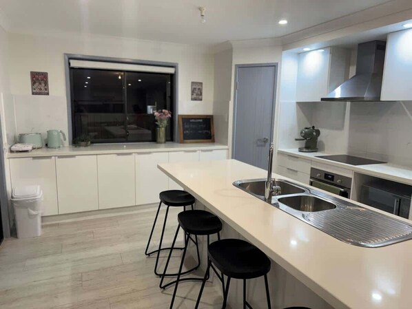 A modern kitchen with a large island, bar stools, a built-in oven, and a window.