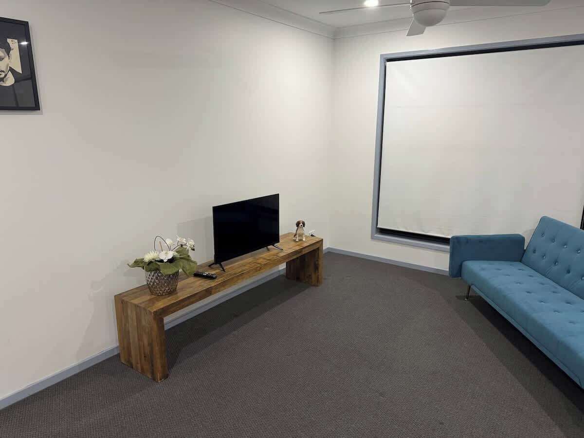 Quarto com televisão de tela plana sobre um banco de madeira, um sofá azul e uma janela grande.