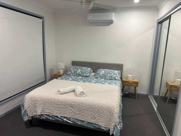 A hotel room with a bed, bedside tables, a mirror, and an air conditioning unit.