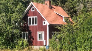 A red wooden house with a sloped roof, surrounded by dense greenery.