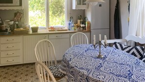 A kitchen with white cabinets, a microwave, a sink, and a window with a view of greenery. There is a table with a patterned tablecloth and candles.