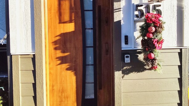 Una puerta de madera con un ventanal, una placa con un número y un arreglo floral.