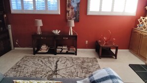 Una sala de estar con sofá, mesa de centro, alfombra y dos ventanas con persianas.