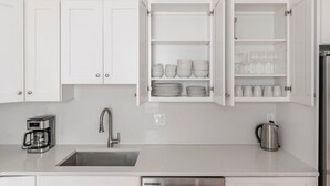 Una cucina moderna con mobili bianchi, un lavello in acciaio inossidabile, una macchina per il caffè e un bollitore.