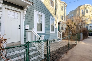 A two-story residential building with a front door, a small porch, and a chain-link fence. - Blueground | Riverside, washer, nr Charles River (Cambridge)